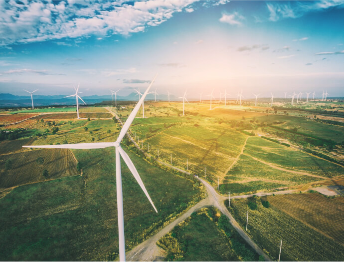 Veterné turbíny pôvabne bodkujú zelenú krajinu pod polojasnou oblohou pri západe slnka, kde je zachytená krása energie prírody, čo možno inšpiruje využitie fpoho poukážky na prijatie trvalej udržateľnosti.