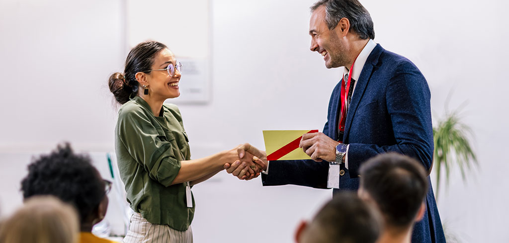 Žena sa usmieva, keď dostáva obálku, odmenu a podanie ruky od manažéra.