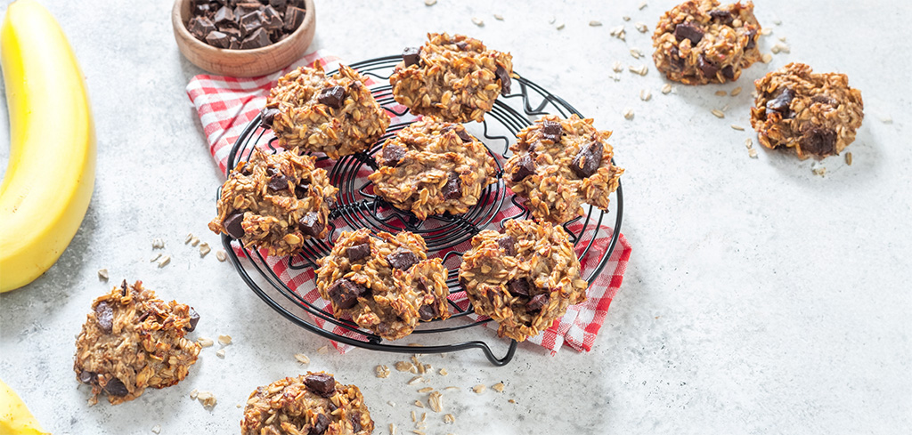 Ovsené sušienky s kúskami čokolády na chladiacej mriežke, obklopené banánmi a kúskami čokolády - ideálne pre tých, ktorí chcú túto sviatočnú sezónu vyskúšať vianočné recepty za stravenku.