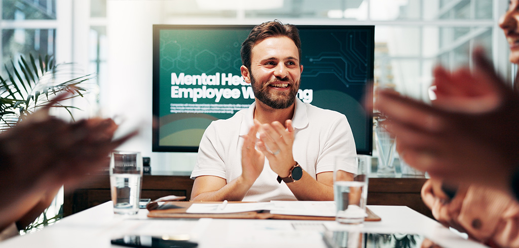 Muž sa usmieva počas stretnutia o duševnom zdraví zamestnancov a pohode zamestnancov, ostatní tlieskajú.