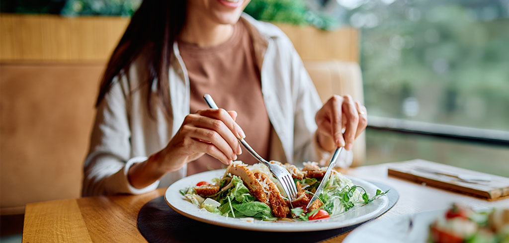 Žena si vychutnáva čerstvý šalát v reštaurácii, dbá na vyvážené stravovacie návyky.