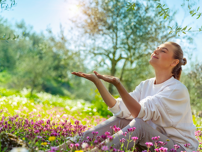Žena sa usmieva a relaxuje na slnečnom poli s poľnými kvetmi, obklopená zeleňou a stromami - zachytáva bezstarostného ducha jarnej súťaže fpoho.