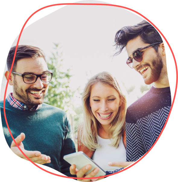 Traja priatelia sa usmievajú a spoločne pozerajú na smartfón vonku počas slnečného dňa.