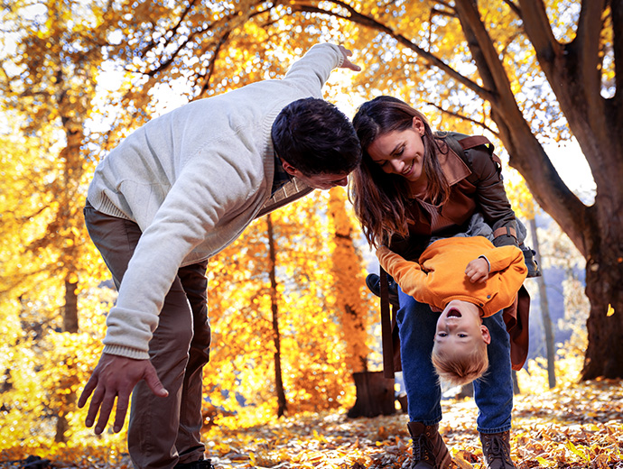 Rodičia hrajúci sa so svojím dieťaťom v jesennom lese, obklopení farebným lístím.