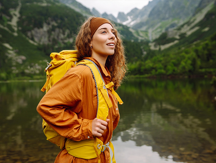 Žena s turistickým batohom pri horskom jazere, usmieva sa na scenériu a užíva si dobrodružstvo vďaka rekreačným poukazom.