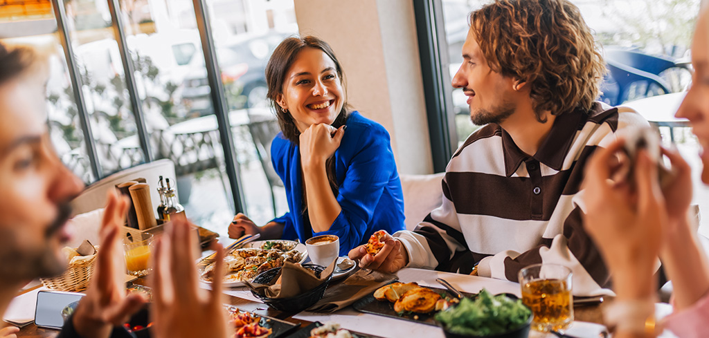 Kolegovia si užívajú zvýšené stravné a vychutnávajú si jedlo v reštaurácii, usmievajú sa a rozprávajú sa pri stole.